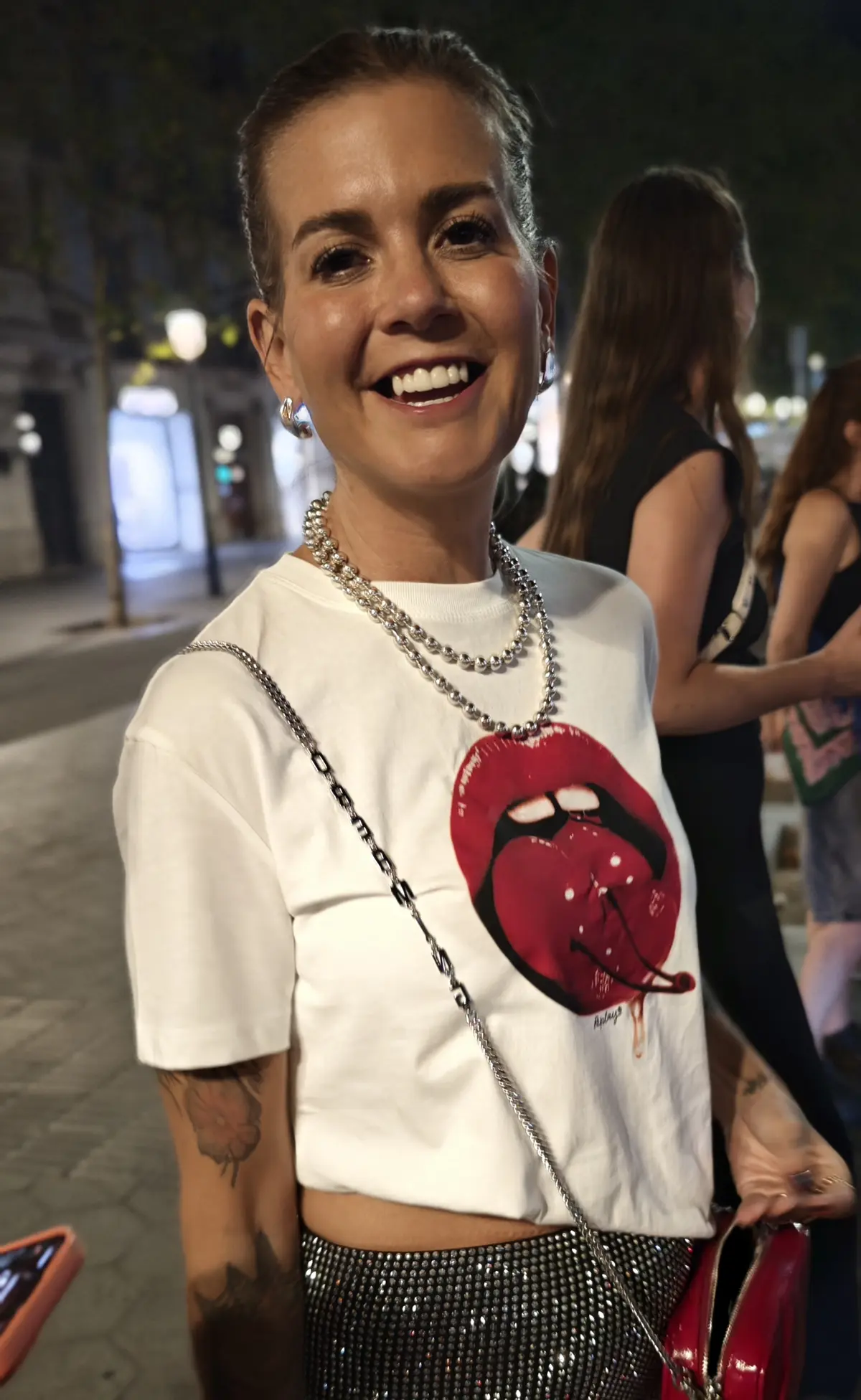 Cortnie smiling on a city street at night in a red lips tee and sparkling skirt